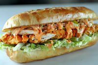 Crispy fried chicken sandwich with fresh lettuce and sauce on crusty bread roll, perfect for restaurant menus and food advertising campaigns.