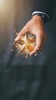 Businessman hand holding glowing golden star with magical light effects representing excellence, achievement, success, quality rating and premium service.