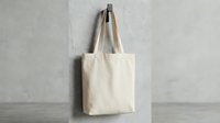 Natural cotton tote bag hanging on concrete wall, eco-friendly reusable shopping bag mockup for branding and promotional designs on neutral background.