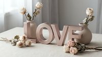 Decorative LOVE letters in soft rose gold tones with dried roses and ceramic vases on a linen table, romantic home decor concept.