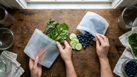 Hands holding clear food storage containers with fresh vegetables and berries on wooden table, promoting meal prep and healthy eating organization for kitchen and lifestyle content.