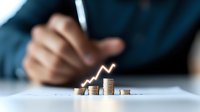 Growing stack of coins with upward trending arrow graph, business person analyzing financial data in background, representing investment growth and profit increase.