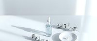 Minimalist skincare serum bottle with dropper on white surface with natural shadows and cosmetic accessories for beauty product photography.