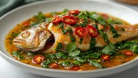 Steamed whole fish with soy sauce, chili peppers and fresh herbs in traditional Asian style cooking. Healthy seafood dish with vibrant garnishes and aromatic broth.