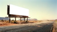 Empty white billboard on desert highway at sunset with dramatic sky and mountain landscape for outdoor advertising campaigns.