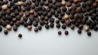 Black peppercorns scattered on white background, creating natural border design with varied tones and textures. Fresh aromatic spice composition for culinary concepts.