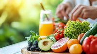 Fresh organic produce with avocado, citrus fruits, berries and vegetables arranged on wooden surface. Orange juice glass in background. Natural lighting and bokeh effect.