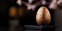 Ornate copper-colored Easter egg with intricate floral pattern on dark background with soft bokeh lights. Luxury seasonal celebration concept.