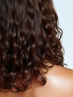 Close-up view of dark brown curly wavy hair cascading down bare shoulders, showing natural texture and shine against white background.