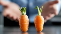 Fresh organic carrots with green tops on dark background, minimalist food composition with blurred hands. Healthy eating and vegetable concept.