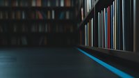Dark library interior with rows of books on shelves, illuminated by mysterious blue light creating moody atmosphere for education and knowledge concepts.