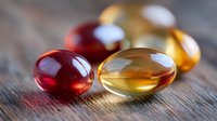 Vitamin supplements and fish oil capsules in red and golden colors on wooden surface with natural lighting, macro photography for health concepts.