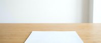 Wooden table top with white blank paper sheet on natural wood surface, isolated on white background for design mockups.