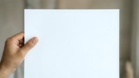 Person of African descent holding blank white paper sheet against neutral background for mockup and branding purposes.