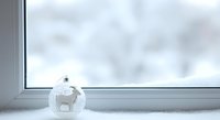 Snow globe with white polar bear figurine sitting on winter window sill with snowy blurred background, seasonal decoration for holiday displays and festive home decor.