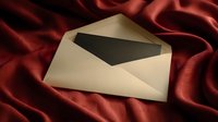 Open cream envelope with black card on luxurious burgundy satin fabric, creating elegant contrast for wedding invitations or formal announcements.