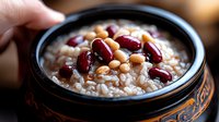 Creamy rice porridge topped with mixed beans in traditional ceramic bowl, close-up view showing texture and garnish. Comfort food styling for menu design.