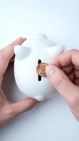 Hands inserting penny coin into white piggy bank for savings and financial planning concepts on clean background.