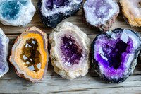 Collection of colorful crystal geodes and mineral specimens with purple amethyst and orange citrine formations on rustic wooden surface for geology education.