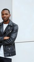Young African American man wearing black leather jacket and white shirt, arms crossed, standing against white wall. Portrait for fashion, lifestyle, and advertising use.