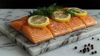 Fresh raw salmon fillet with lemon slices, dill and peppercorns on marble cutting board against dark background. Culinary preparation concept.