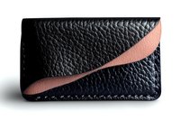 Stylish black leather cardholder with curved pink accent stripe features textured grain pattern and minimalist design for modern business accessories.