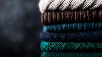 Stack of folded knitted winter sweaters in different colors from gray to turquoise on dark background, seasonal clothing and fashion concept.