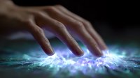 Mystical glowing energy emanates from human finger touch on dark surface with ethereal blue and purple light effects creating magical supernatural atmosphere.