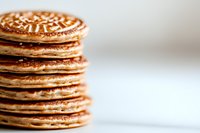 Stack of golden brown pancakes with crispy edges photographed in macro view against light background, showing delicate texture and layers of breakfast treat.