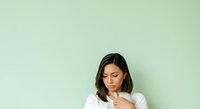 Young woman with dark hair and South Asian ethnicity wearing white casual shirt, looking down thoughtfully with hand near chin against soft mint green background, suitable for lifestyle and wellness content.