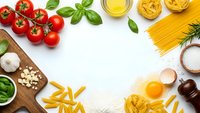 Fresh pasta ingredients arranged on white background with tomatoes, basil, olive oil, eggs and various noodles for Italian cooking recipes.