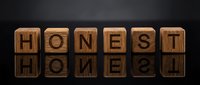 Wooden letter blocks spelling HONEST on dark reflective surface. Business ethics, integrity and trust concept for corporate communications and branding.