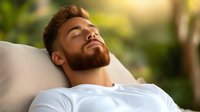 Young bearded man with closed eyes relaxing outdoors on white cushion, expressing serenity and mindfulness in natural sunlit environment.