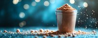 Creamy chocolate milkshake or smoothie in glass cup with cocoa powder topping against blue bokeh background.