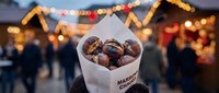 Roasted chestnuts in paper cone at festive Christmas market with warm bokeh lights and holiday atmosphere creating cozy winter evening scene.