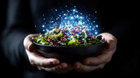 Fresh green salad in dark ceramic bowl with magical glowing sparkles and light effects floating above, hands holding dish against black background.
