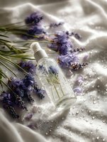 Fresh lavender flowers and glass bottle with essential oil on white fabric with water drops, natural aromatherapy and spa wellness concept.