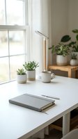 Minimalist home office workspace with notebook, coffee cup and succulents on white desk near window with natural light for productivity and focus.
