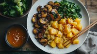 Asian inspired vegetarian bowl with crispy gnocchi, sauteed mushrooms, steamed kale and sweet chili sauce on rustic wooden table. Healthy plant based meal.