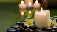 Spa wellness scene with burning candles, tropical flowers and hot stones creating peaceful relaxation atmosphere for massage therapy and meditation.