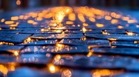 Glowing orange lights reflected on wet cobblestone street surface creating magical bokeh effect at night, atmospheric urban scene with rain puddles.