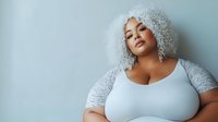 Young woman with voluminous platinum curly hair wearing white top against light blue background, showcasing modern beauty and confidence.