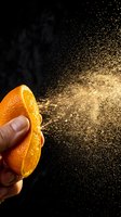 Hand squeezing fresh orange half with juice spray bursting against black background. Citrus fruit, freshness, and natural vitamin concept for food and beverage design.