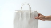 Hand holding white paper shopping bag with handles on clean background for retail packaging and eco-friendly commerce applications.