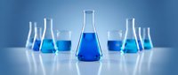 Laboratory glassware with blue chemical solutions on white surface against gradient blue background for scientific research and education.