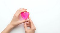 Hands holding bright pink heart shape on white background for love, romance, charity and healthcare concepts.