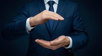 Professional businessman in navy suit making protective gesture with hands showing security and insurance concept for corporate presentations.