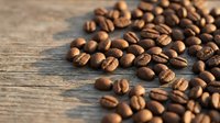 Roasted coffee beans scattered on rustic wooden surface with natural lighting for cafe menu design and beverage marketing materials.
