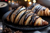 Fresh baked chocolate striped croissant with powdered sugar on dark plate against blurred bokeh lights background, close up view of French pastry.