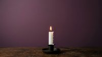 Lit white candle in black holder on wooden surface against purple background, suitable for spirituality, meditation, and home decor projects.